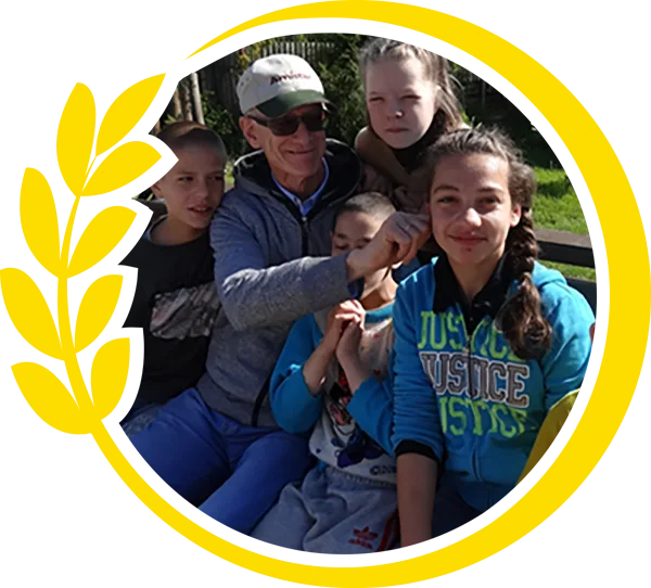 Round photo Mark sitting with children on a bench outside surrounded by yellow circle of wheat